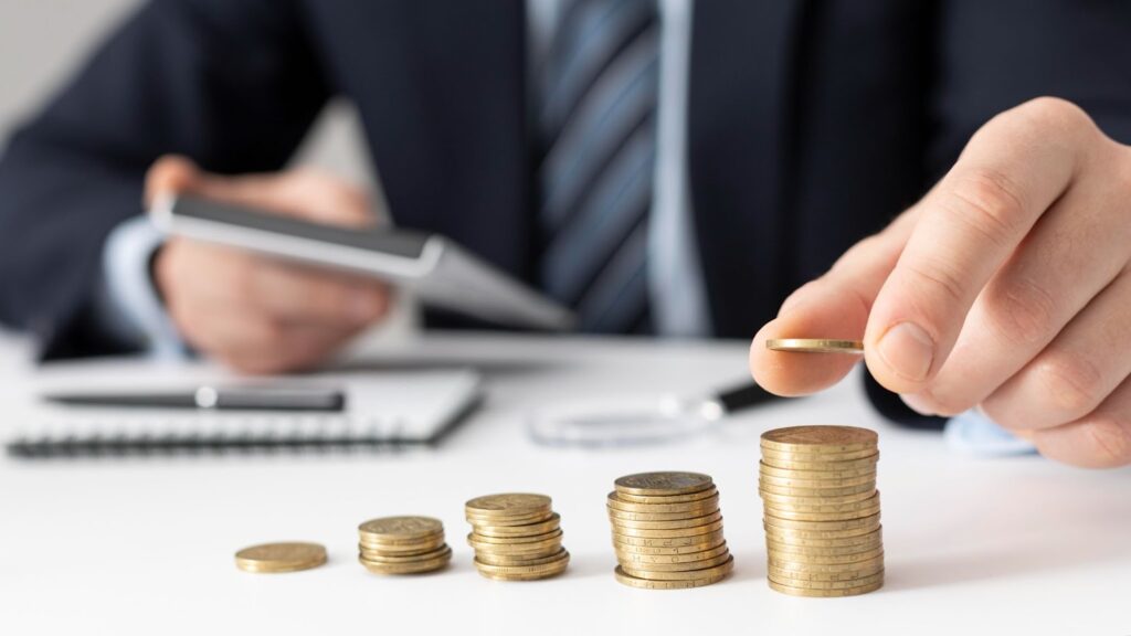 Close up of man stacking coins while holding a calculator